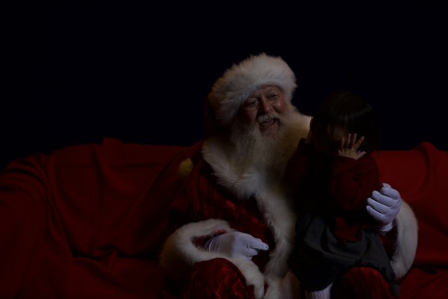 A Festive Santa Claus Taking a Break on a Red Couch with a Child