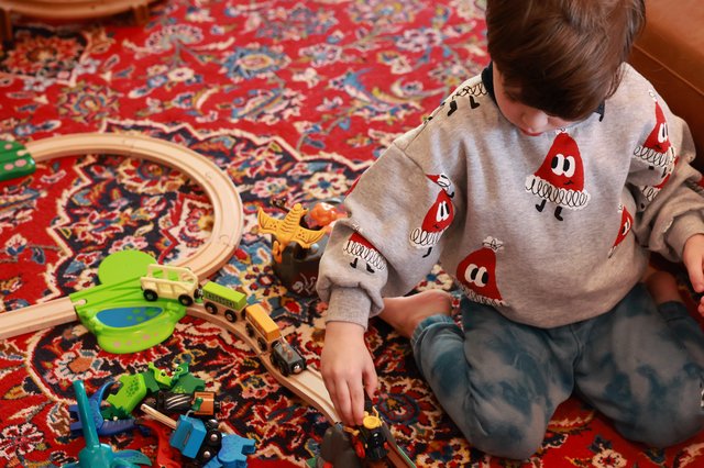 Child Playing with Wooden Train Set on Patterned Rug