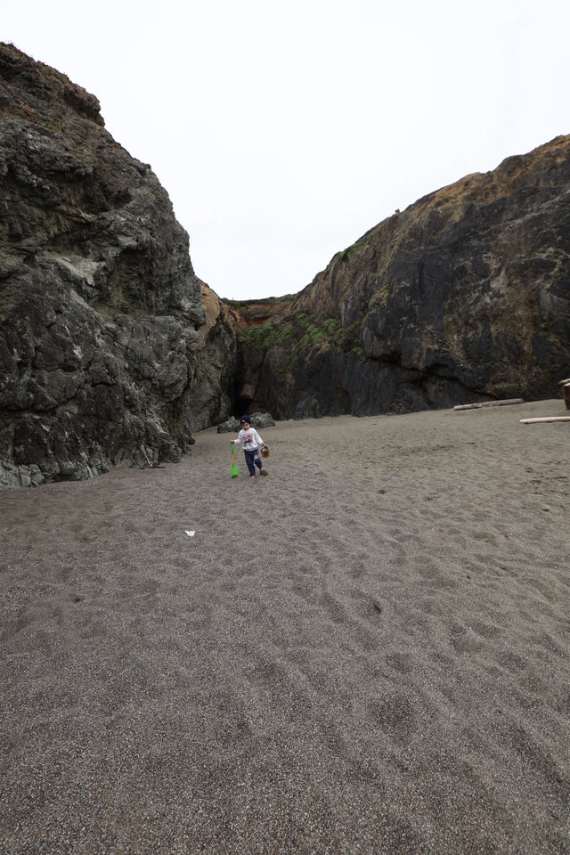 Child Explorer Between Sea Cliffs on Dark Sand Beach