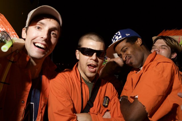 Three men in orange jackets with baseball caps and sunglasses