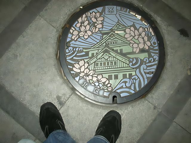 Manhole Cover Featuring a Building Painting in Osaka