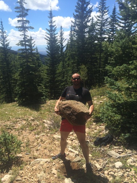 Man holding a large rock in the wilderness