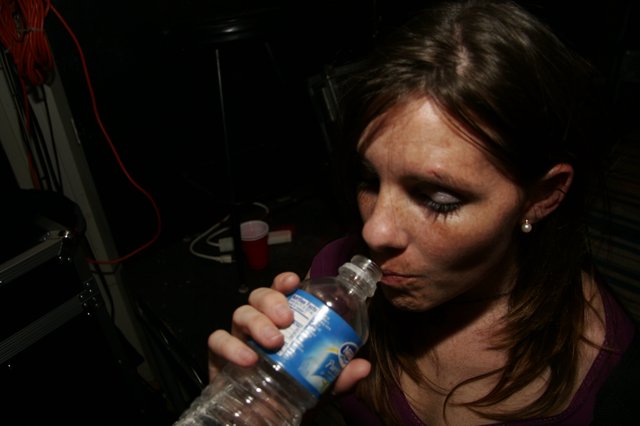 Woman Drinking Water Bottle in Dark Venue