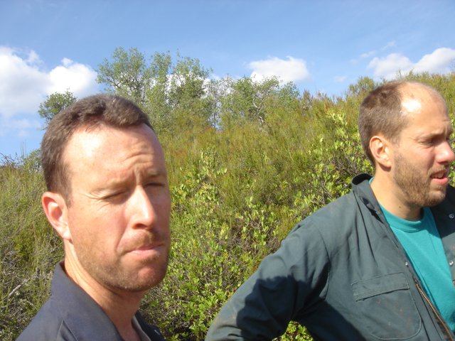 Two Men Standing in Front of a Bush