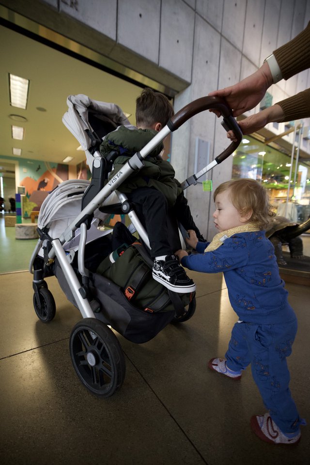 Toddler Helping Parent Push Stroller at Indoor Venue