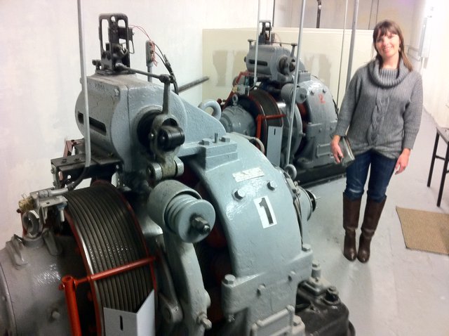 Woman Poses Beside Historic Elevator Machine Room Equipment