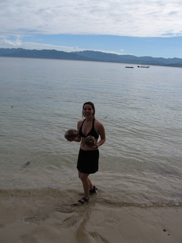 Smiling Woman Holding Coconuts on Fijian Shore