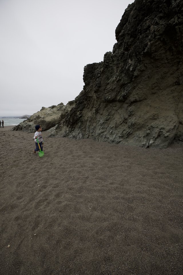 Child Explores Dark Sand Beach Beside Dramatic Cliffs