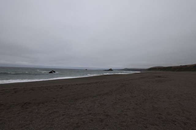Moody Overcast Beach with Dark Sand and Ocean Rocks