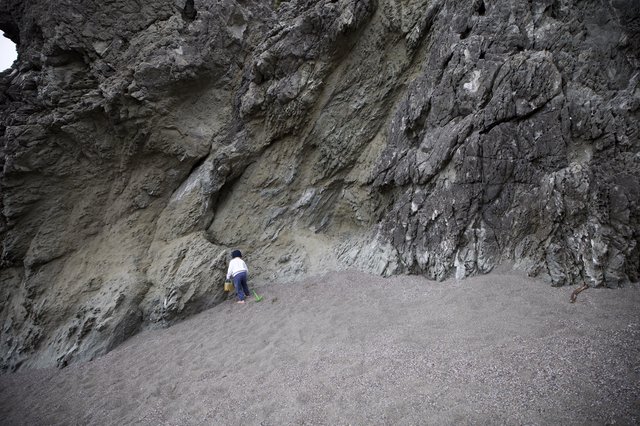 Small Child Explores Towering Sea Cliff at Low Tide