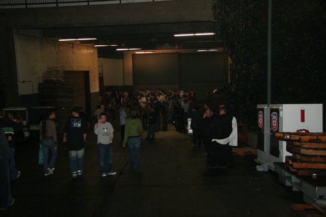 Group of People in a Parking Lot Caption: John Petrucci (center) stands among a crowd of 20 people wearing jeans and various accessories, outside a factory building in New York on New Year's Eve of 2005.