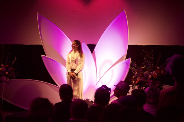 Woman in Elegant Purple Dress Performs on Stage with Flower Arrangement