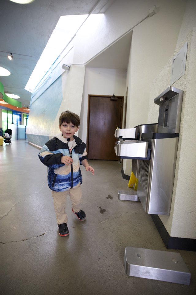 Young Boy Walking Past Water Fountain in School Hallway