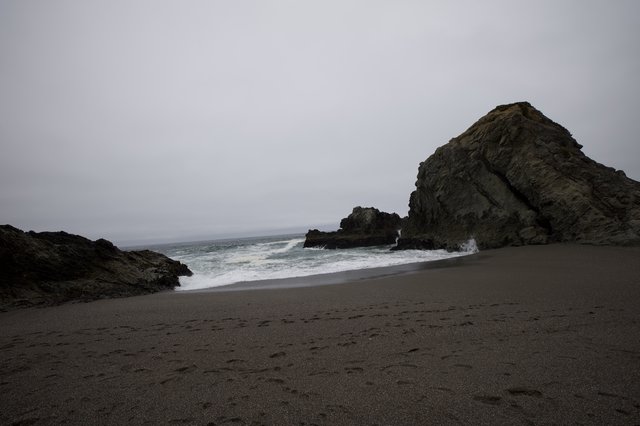 Moody Coastal Cove with Dark Sand and Sea Stacks