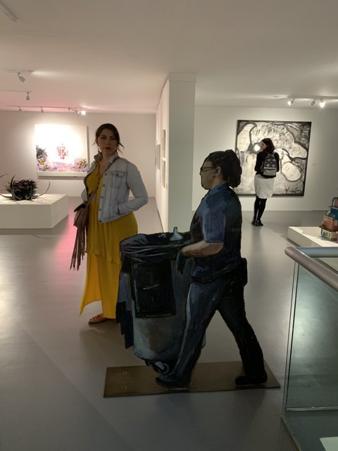 Woman carrying a trash can through an art gallery