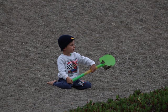 Young Boy Playing with Shovel on Sandy Beach