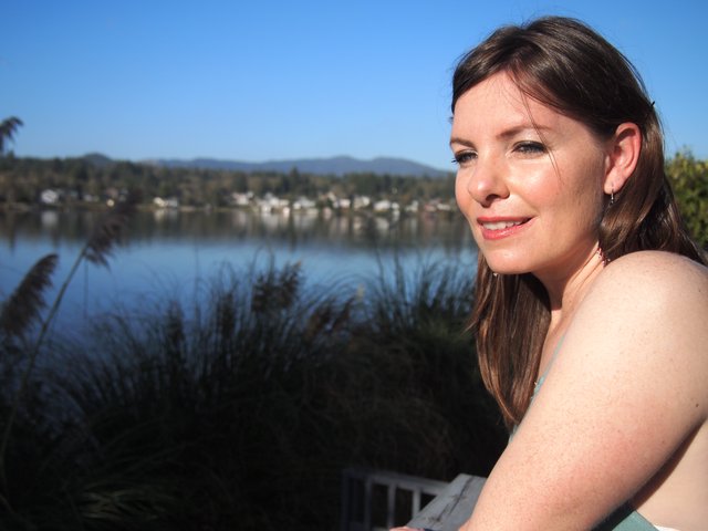 Woman Smiling by a Tranquil Lakeside on Sunny Day