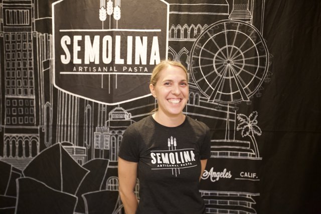 A Happy Woman Stands in Front of a Semolina Sign