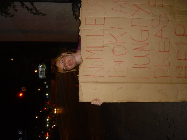 Woman Holds Humorous Homeless Cardboard Sign at Night