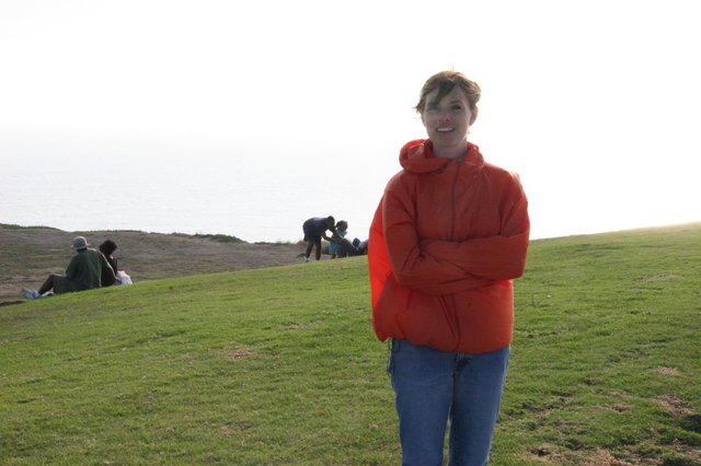 Woman in Red Hoodie on Coastal Hillside at Dusk