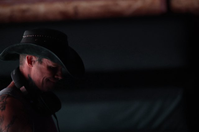Tattooed Performer in Black Cowboy Hat Under Stage Lights