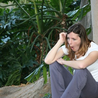 Surprised Woman Crouching by Tropical Garden Wall