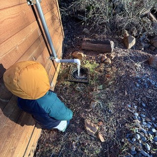 Child Inspects Rainwater Drainage System Beside Cabin