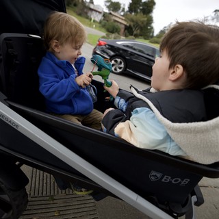 Two Young Children Sharing Toys in Double Stroller