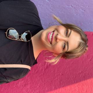 Smiling Woman in Sunglasses Poses in Front of Colorful Wall