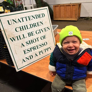 Joyful Toddler at Coffee Shop with Humorous Warning Sign