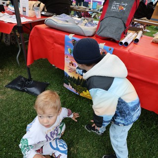 Curious Toddlers Explore Balloon Festival Merchandise Table
