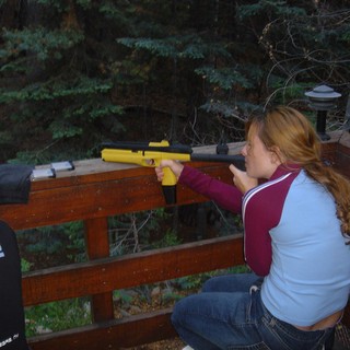 Young Woman Aiming Yellow Air Pistol on Wooden Deck
