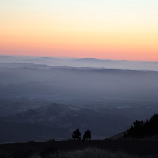 Two Silhouettes Watching Sunset Over Layered Mountain Valleys