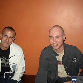 Two Men Sitting in Front of an Orange Wall