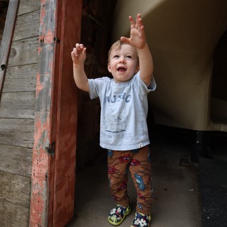 Joyful Toddler Reaching Up in Rustic Doorway