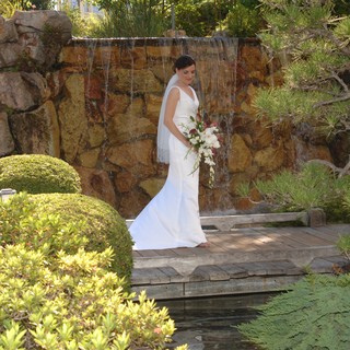 Bride Stands Elegant Before Stone Waterfall Garden