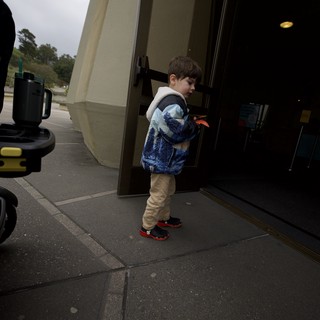 Young Boy Peering Through Glass Storefront Door