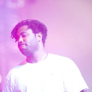 Sampha's Time to Shine        Caption: British singer-songwriter Sampha, wearing a white T-shirt and purple undershirt, takes center stage and beams with happiness while performing at Coachella 2017, with the spotlight illuminating his face and microphone.