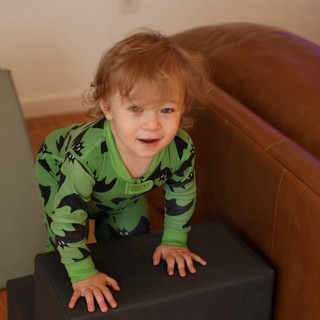 Toddler in Green Dinosaur Pajamas Playing on Ottoman