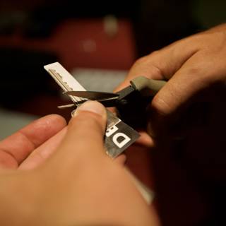 Precise paper cutting Caption: A person's fingers and hand skillfully wield scissors to cut through a piece of paper with precision. In the background, a credit card and text can be seen on a table. Photograph taken in 2008 at pre defcon.