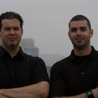 Two Men in Black Shirts Pose in Hazy Outdoor Scene