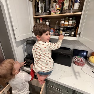 Brothers Reaching for Spices in Kitchen Cabinet