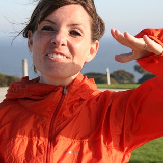 Woman in Orange Jacket Poses by the Coast