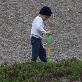 Young Boy Explores Rocky Beach with Stick