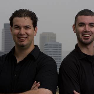 Two Happy Men in Black Shirts Pose for a Cityscape Portrait