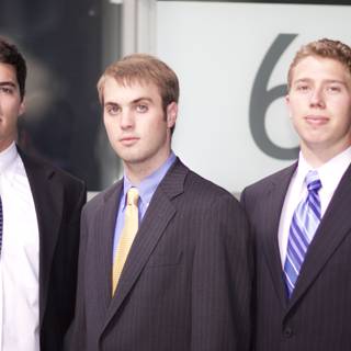 Three Men in Suits Pose in Front of a Sign