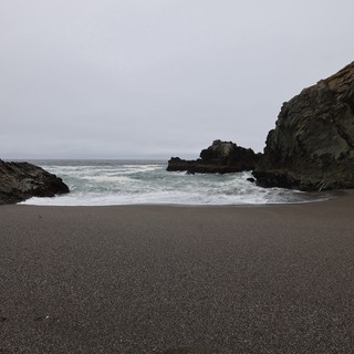 Secluded Cove with Dark Sand and Crashing Waves