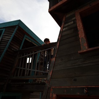 Child Peering from Weathered Wooden Balcony at Dusk