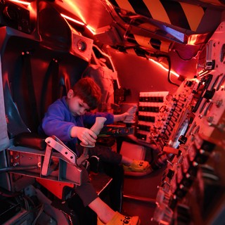 Young Visitor Explores Spacecraft Interior Under Red Emergency Lighting