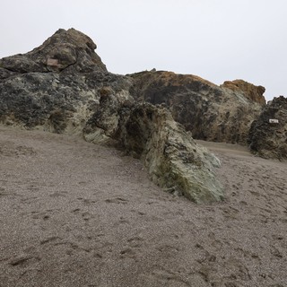 Ancient Coastal Rocks Emerging from Gray Sandy Beach